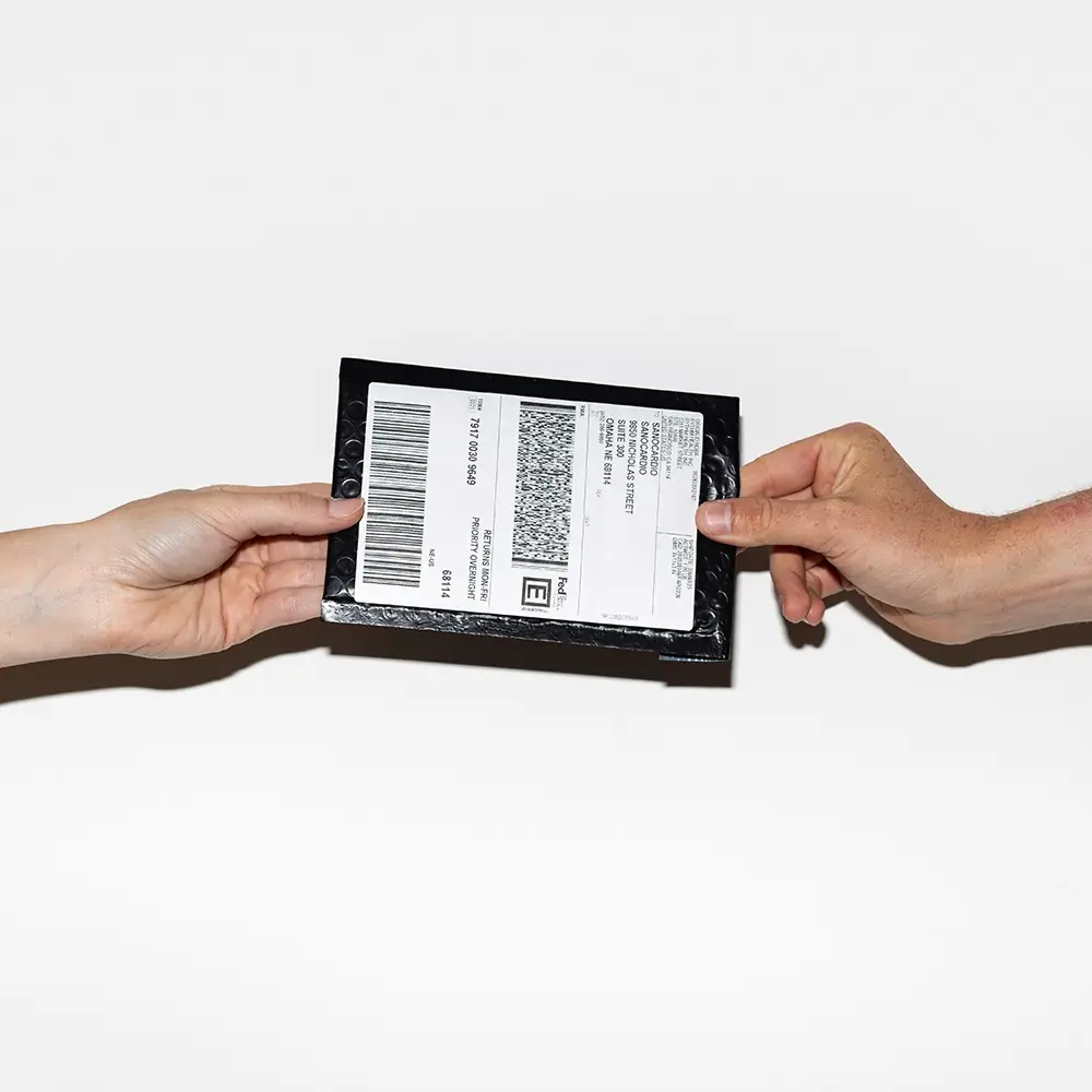 Hands exchanging a Rythm Health at-home blood test kit for laboratory analysis.