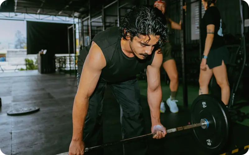 Muscular man in a black shirt gripping a barbell at a gym, focused and mid-lift.