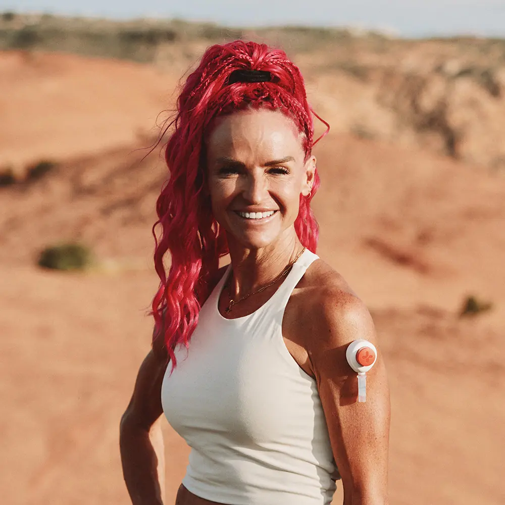 Ashley P outdoors in a desert landscape wearing a Rythm Health sensor on her upper arm.
