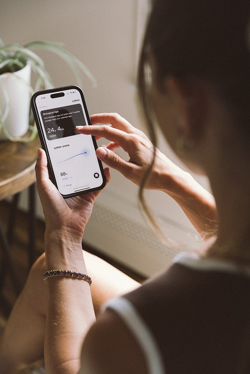 Person holding a smartphone displaying the Rythm Health app, showing a hormone score and health metrics on screen.