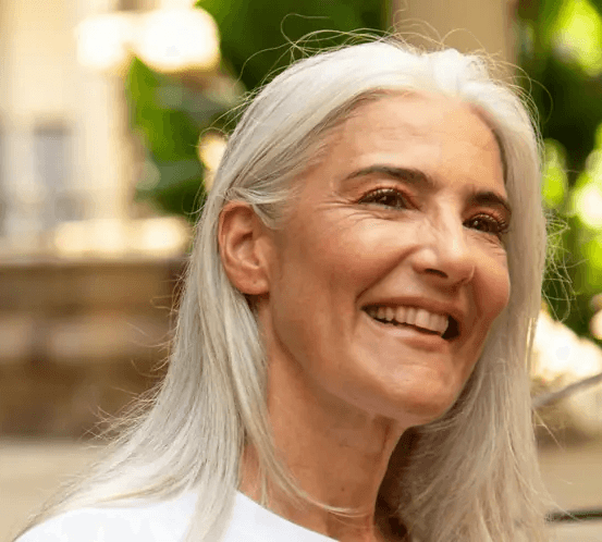 Radiant older woman with silver hair smiling in a sunlit garden.