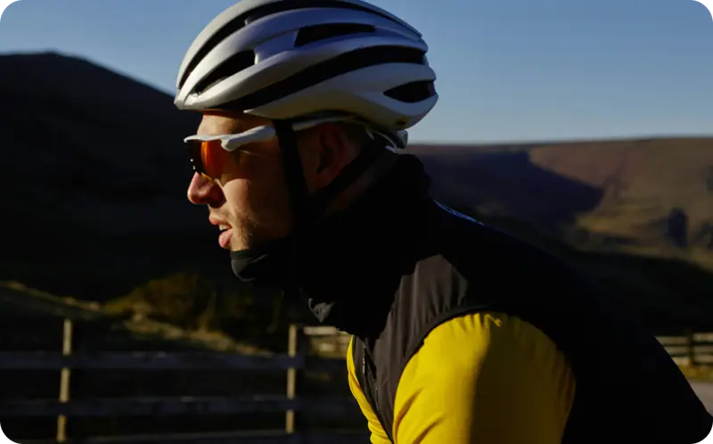 Male cyclist in a yellow and black jersey wearing a white helmet and orange-tinted sunglasses on a mountain road.