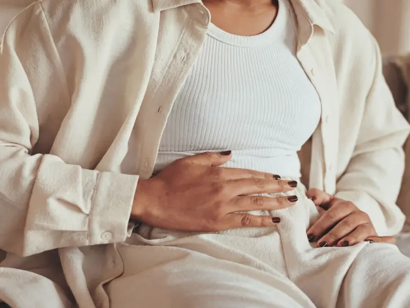 Close-up of a woman’s torso and hands resting on her abdomen, representing internal health and biomarker tracking.
