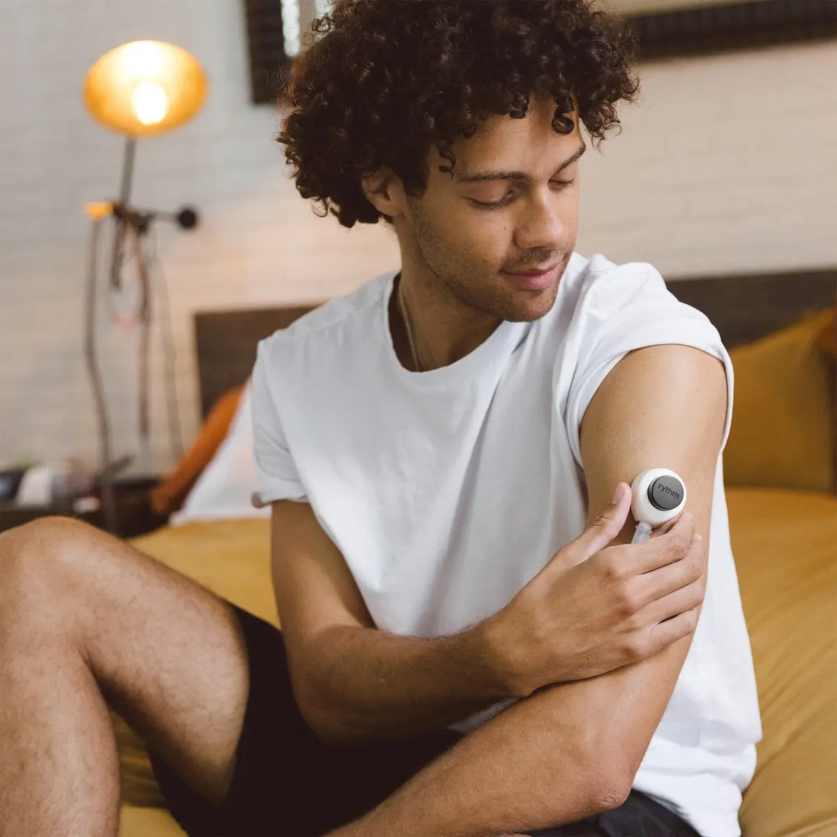 Person applying a Rythm Health wearable sensor to the upper arm for at-home biomarker tracking.