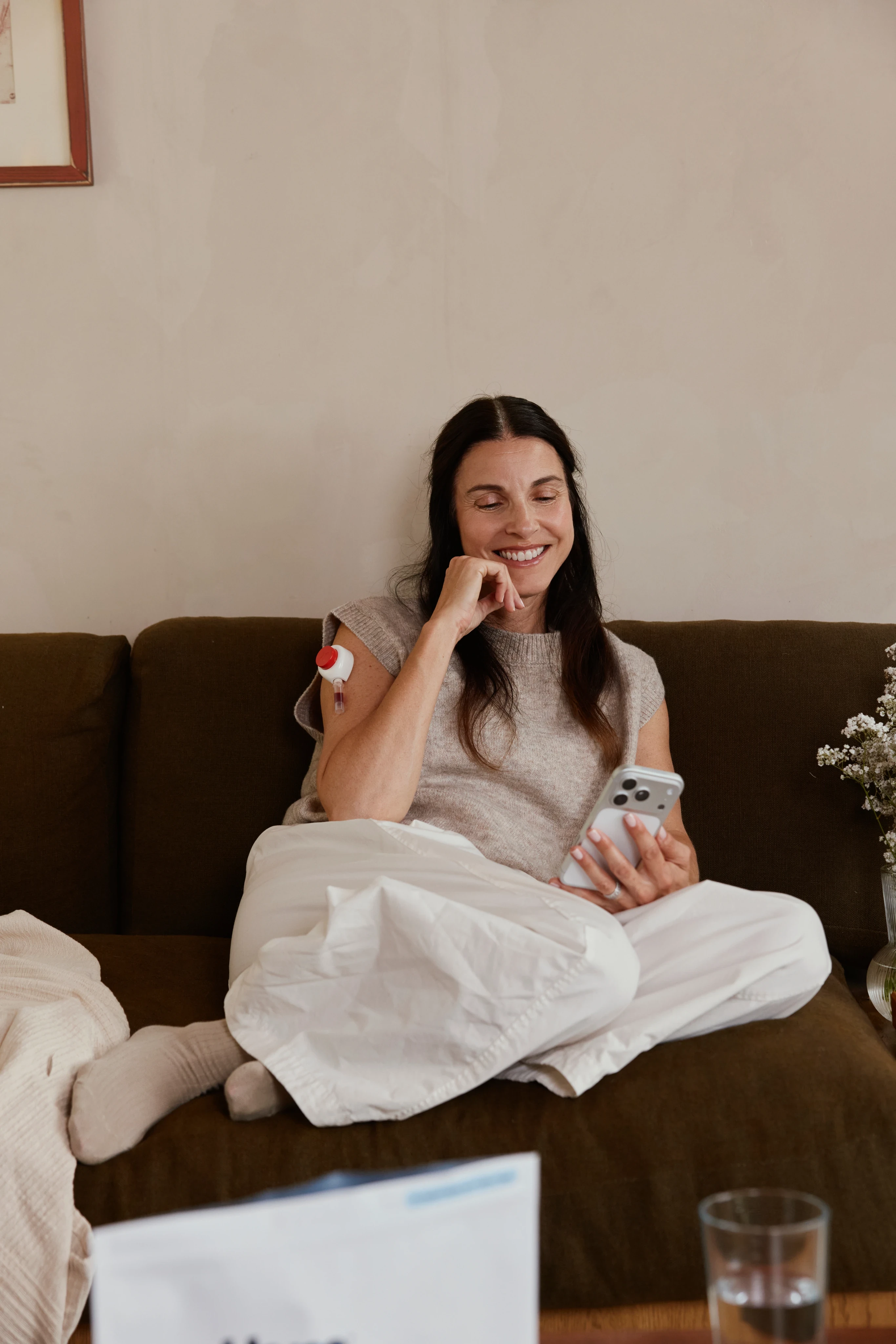 Woman using a Rythm at-home blood collection device on her upper arm, seated indoors in soft natural light, looking down as she applies the device.