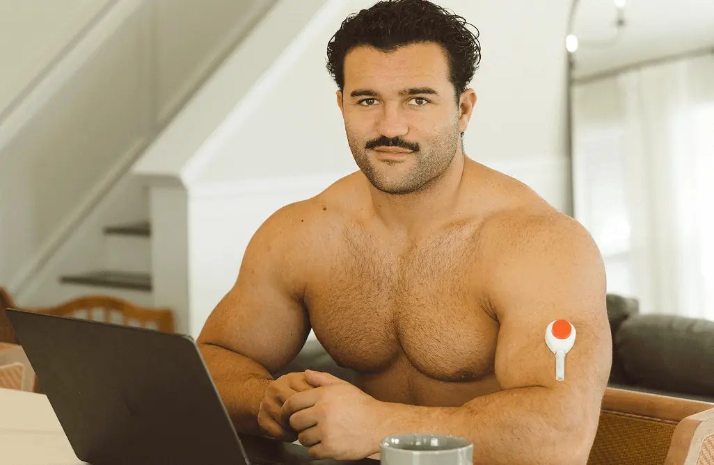 Jam seated indoors working on a laptop while wearing a Rythm Health sensor on his upper arm.